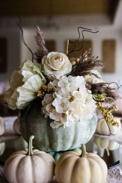 a delicate pastel Thanksgiving centerpiece of a green pumpkin, neutral blooms, berries, dried grasses is amazing