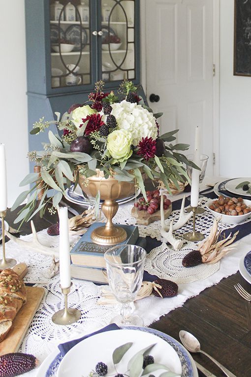 a dramatic Thanksgiving centerpiece of a gold bowl, white and purple blooms, greenery, blackberries and fruit