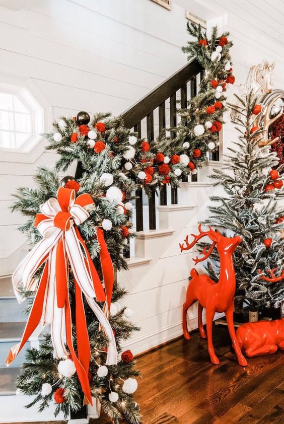 a fantastic Christmas entryway styled with red deer, a flocked tree with red and white ornaments, a lush railing garland with a large red and white bow