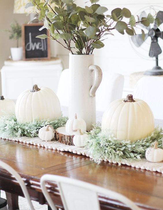 a farmhouse Thanksgiving centerpiece of greenery, white pumpkins and gourds and greenery in a tall jug is awesome