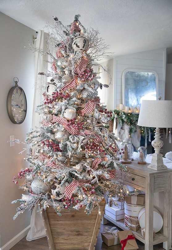 a flocked Christmas tree with oversized white and silver ornaments, red berries and striped ribbons plus lights