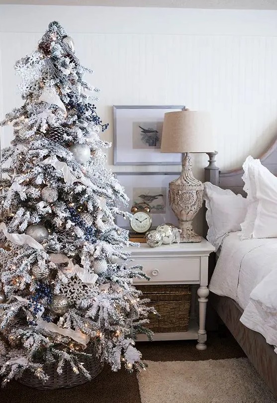 a flocked Christmas tree with privet berries, snowflakes, ribbons, white and silver ornaments and pinecones plus lights is amazing