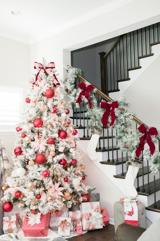 a flocked Christmas tree with red, metallic and white ornaments of various sizes and lights plus snowy greenery and red bows