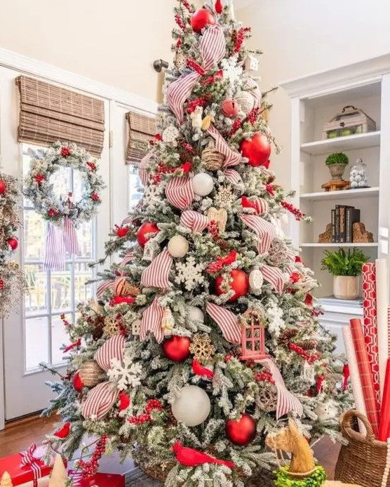 a flocked Christmas tree with white, red and twine ornaments, snowflakes, striped ribbons and berry branches is wow