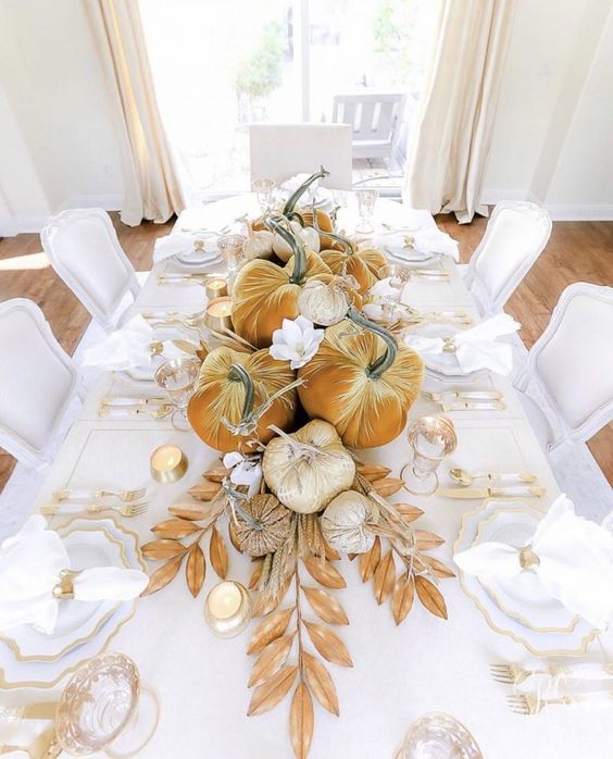 a glam Thanksgiving centerpiece of mustard and metallic velvet pumpkins and faux leaves plus some candles is wow