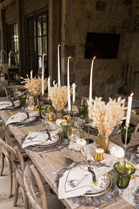 a gorgeous rustic Thanksgiving tablescape with feather placemats, bunny tail centerpieces, tall and thin candles, printed plates and napkins