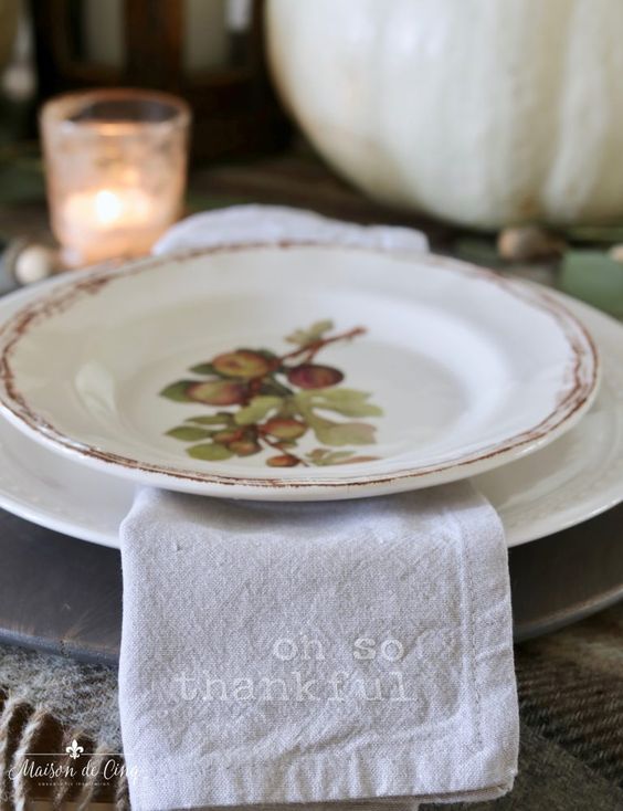 a grey wooden placemat, a white and a fruit printed plate plus a printed napkin are amazing for a cozy Thanksgiving tablescape