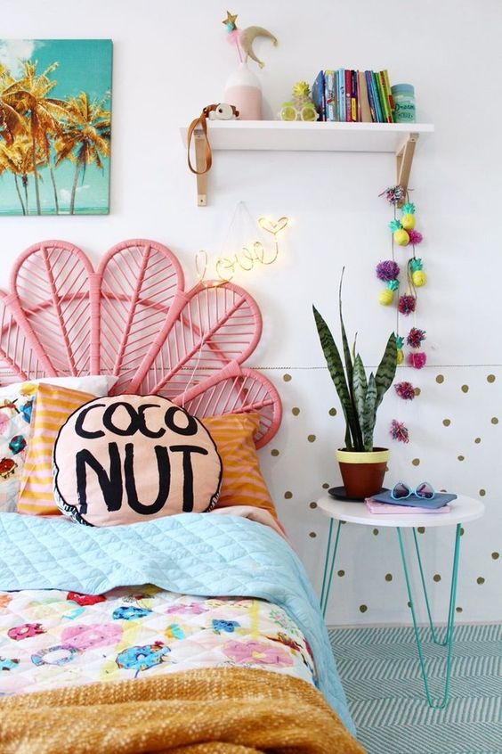 a lovely bright kid's room with a bed with a pink peacock headboard and colorful bedding, a polka dot wall, colorful decor and books
