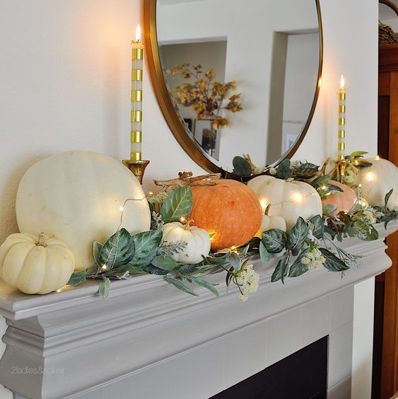 a lovely modern Thanksgiving mantel with greenery, white blooms and large natural pumpkins and candles