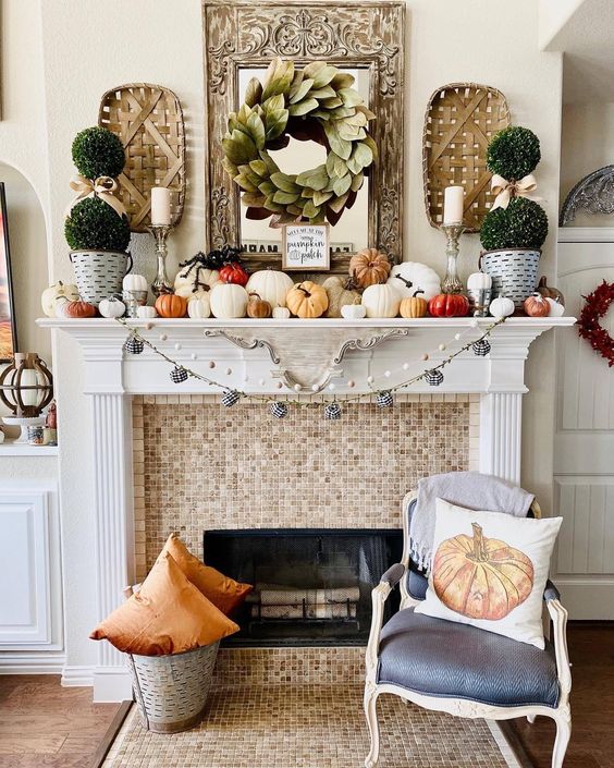 a lovely modern farmhouse Thanksgiving mantel with lots of pumpkins of various sizes, greenery topiaries, a leaf wreath and woden baskets