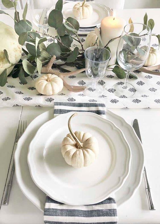 a lovely neutral Thanksgiving place setting with vintage plates, a striped napkin, silver and a small pumpkin on top is cool