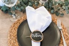 a lovely rustic Thanksgiving place setting with a woven placemat, a black plate, a white napkin, a chalk board wood slice as a place card