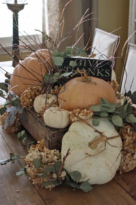 a lush rustic Thanksgiving centerpiece of a wooden box, pumpkins, leaves, dried hydrangeas and lots of twigs