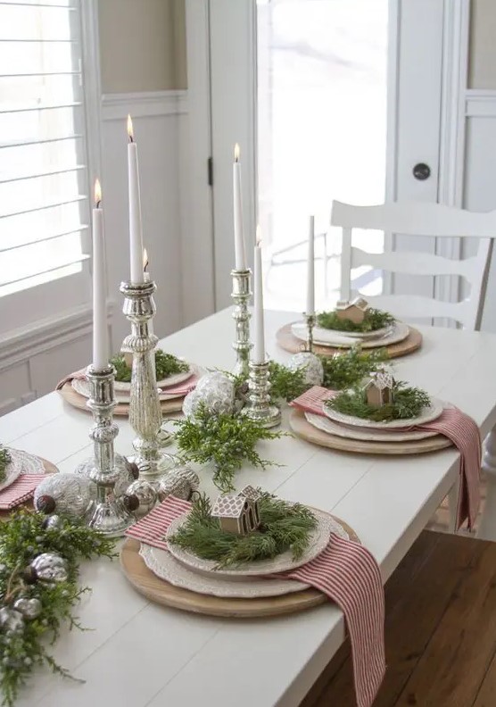 a merry Christmas table with mercury glass candleholders and ornaments, wooden placemats, red and white striped napkins and gingerbread houses