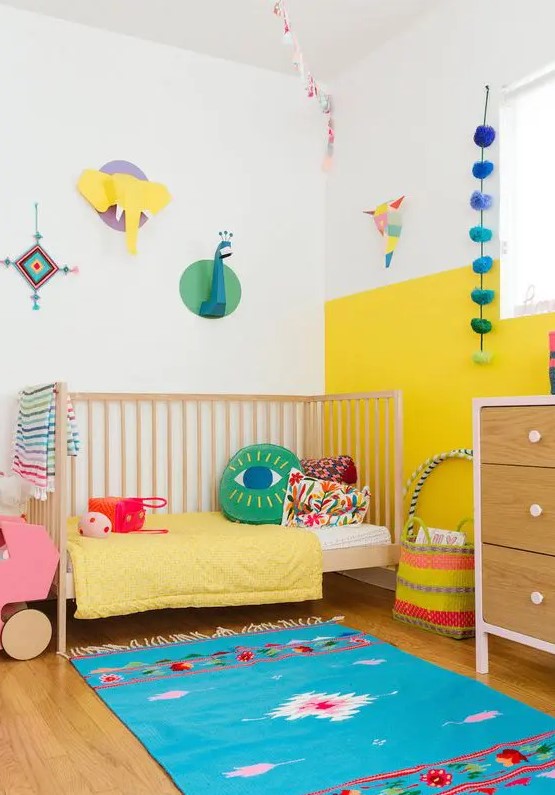 a modern colorful kid's room with a color block yellow and white wall, bright bedding and a rug, cardboard taxidermy and accessories