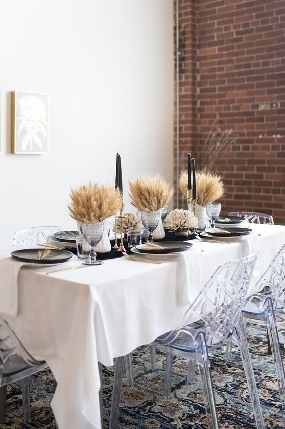 a modern farmhouse Thanksgiving centerpiece of wheat in jugs and black candles in tall gilded candleholders