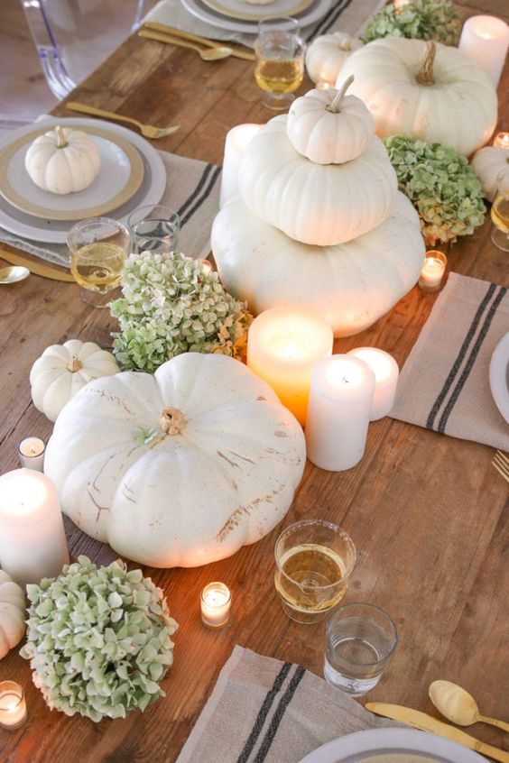 a natural Thanksgiving centerpiece of green hydrangeas, white pumpkins stacked and pillar candles around is amazing