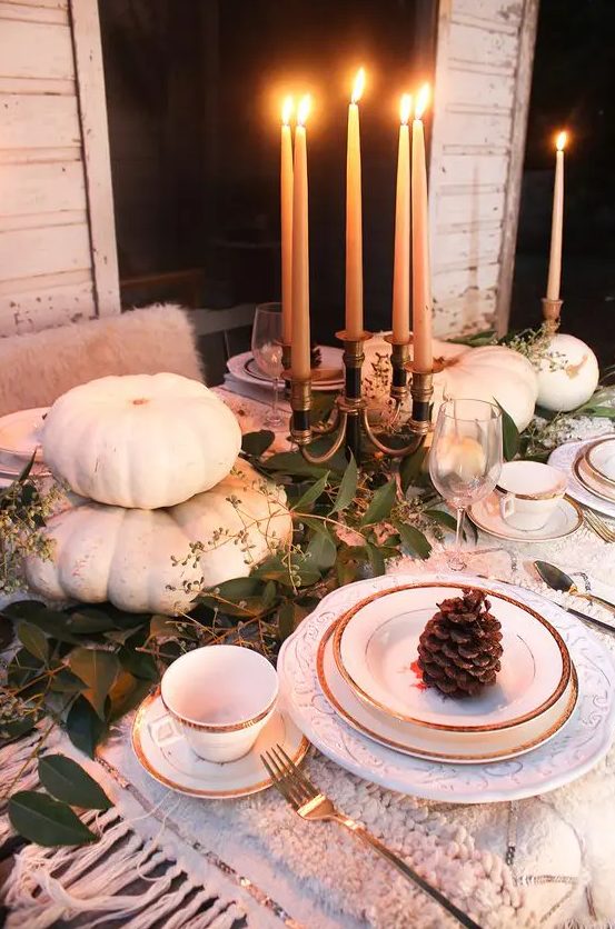 a natural Thanksgiving tablescape with white pumpkins, tall candles and a greenery runner plus pinecones is chic