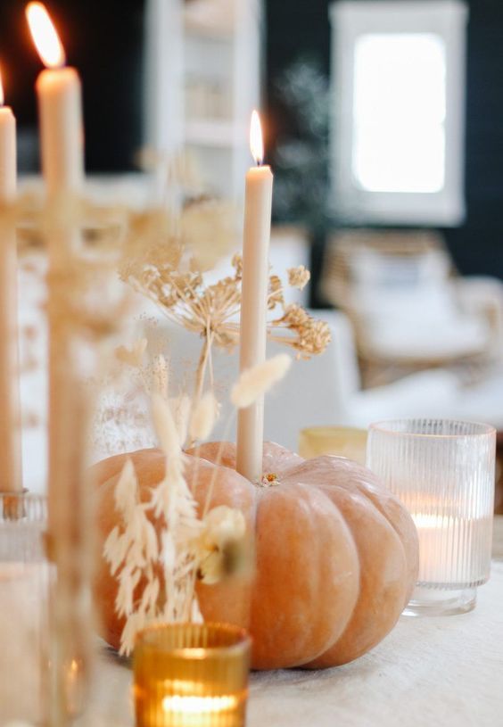a natural pumpkin with a tall and thin candle and lots of grasses plus candles around is a cool decor idea for Thanksgiving