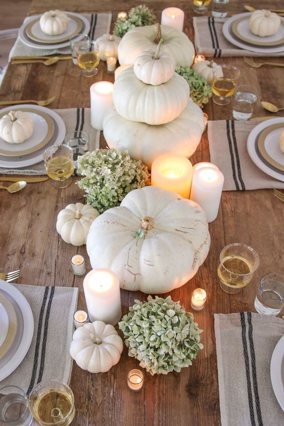 a neutral and natural Thanksgiving centerpiece of green hydrangeas, white pumpkins, candles, small and large ones