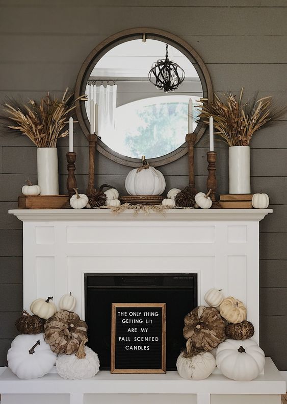 a neutral farmhouse Thanksgiving mantel with wheat, wooden candleholders, some mini pumpkins and large ones at the fireplace