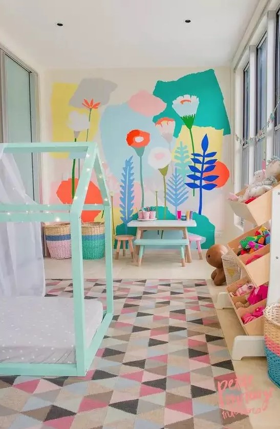 a pastel kid's room with a bright floral wall, a mint house-shaped bed, colorful toys and a bold rug and baskets
