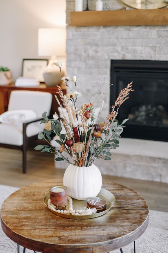 a pretty floral Thanksgiving centerpiece of a white pumpkin, burgundy and white blooms, greenery and dried grass