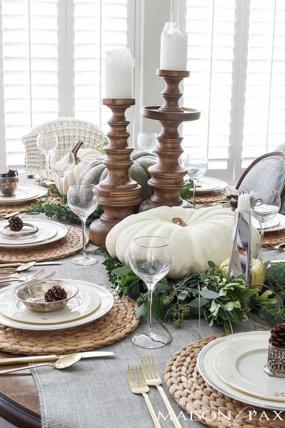a pretty vintage rustic Thanksgiving centerpiece of eucalyptus, large heirloom pumpkins and white pillar candles in wooden candleholders