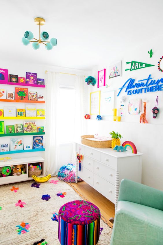 a rainbow-inspired kid's room with colorful ledges and books, a bold gallery wall, a green leather rocker, a colorful pouf
