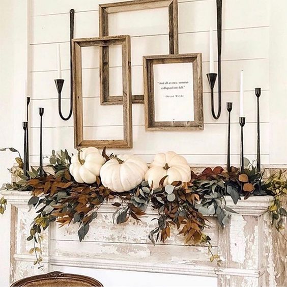 a refined vintage Thanksgiving mantel with lots of greenery and dried leaves, white pumpkins, white candles and empty frames for a farmhouse touch