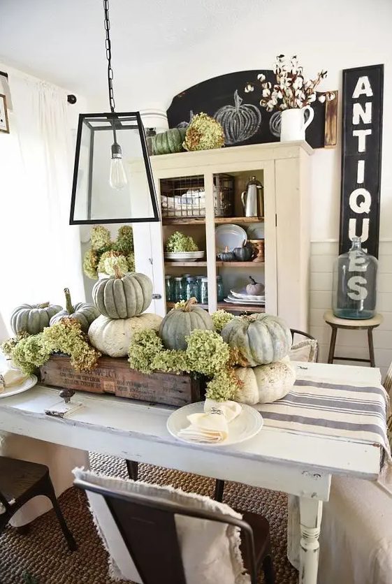 a rustic Thanksgiving centerpiece of a wooden box, green hydrangeas and neutral heirloom pumpkins is a cozy and cool idea