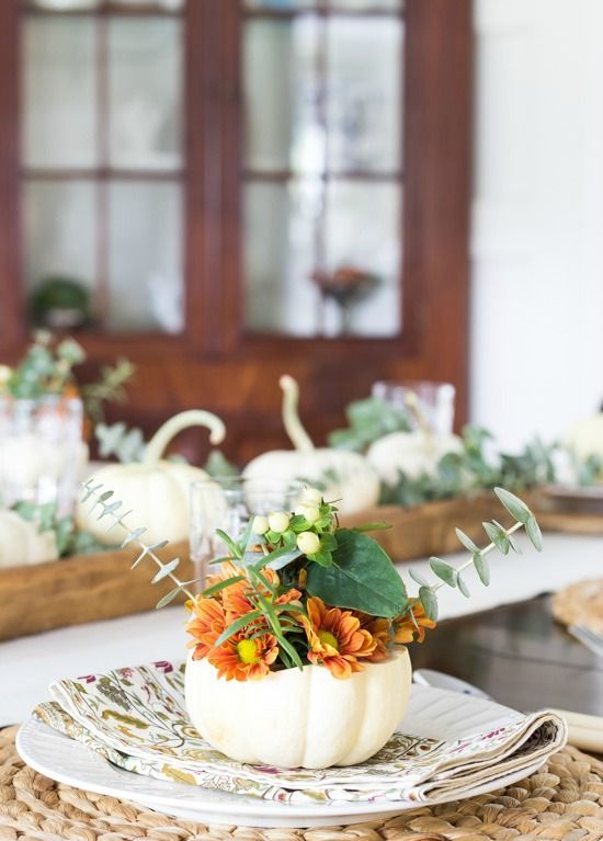 a rustic Thanksgiving place setting with a woven placemat, a printed napkin, a white pumpkin with blooms and greenery