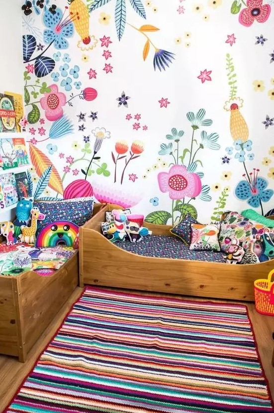 a shared colorful kid's room with a bright floral wall and bold bedding, a bold striped rug and books on the bookshelves