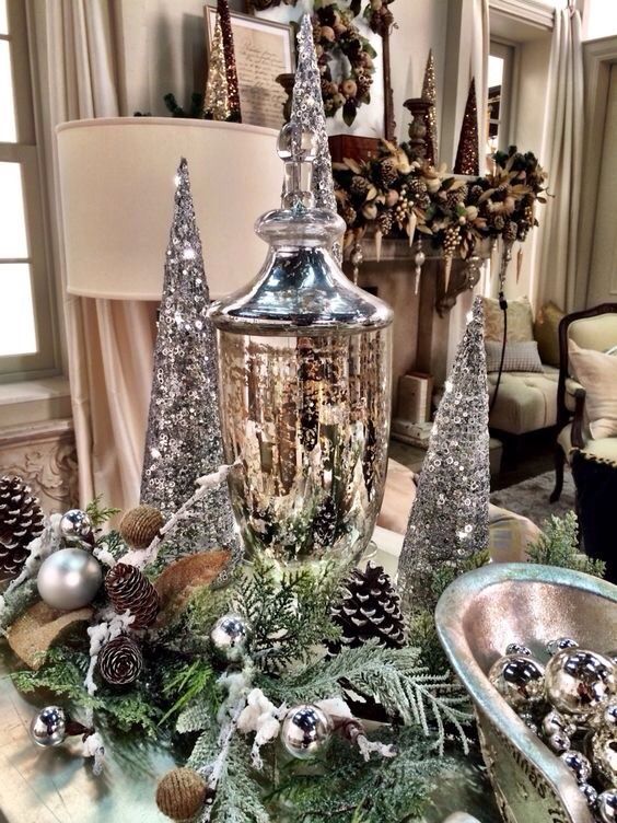 a silver Christmas centerpiece of evergreens, pinecones, silver ornaments, silver sequin cone trees and a mercury glass jar