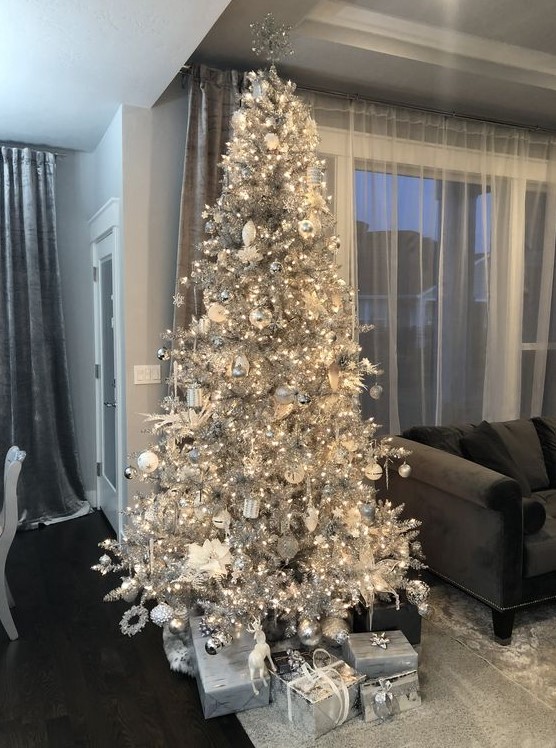 a silver Christmas tree with lights, white and silver ornaments, fabric blooms and silver gift boxes is a stylish and bold idea