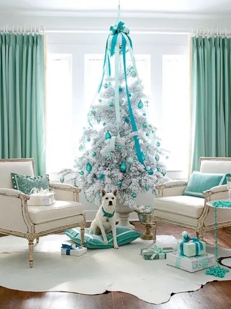 a silver Christmas tree with silver and turquoise ornaments and ribbons and a large suspended bow over the tree