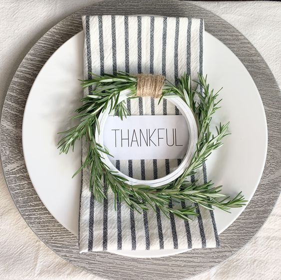 a simple and modern Thanksgiving place setting with a plywood placemat, a white plate, a striped napkin and a greenery wreath