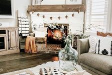 a simple farmhouse Thanksgiving mantel with a pinecone garland, several signs and pillows and a blanket
