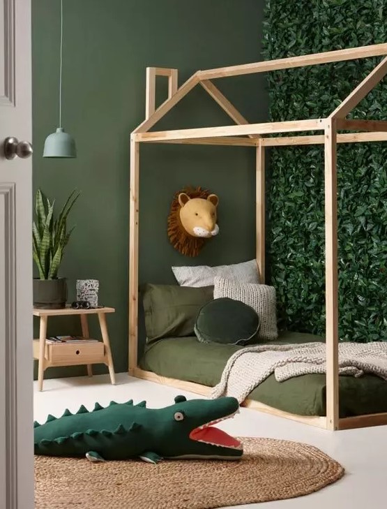 a small jungle kids' room with a faux greenery accent wall, a house-shaped bed with green bedding, a jute rug and a nightstand with plants