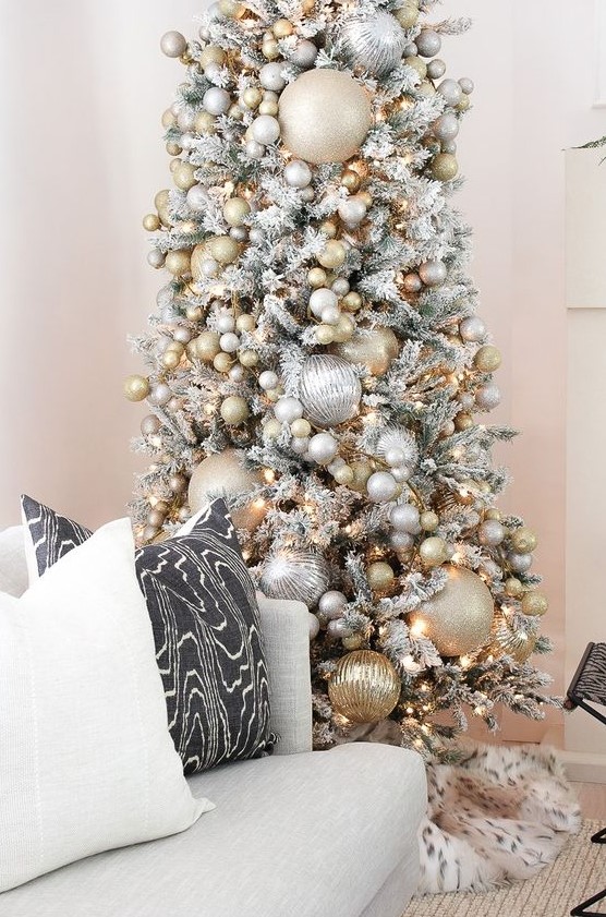 a snowy Christmas tree with oversized and smaller metallic Christmas ornaments plus lights