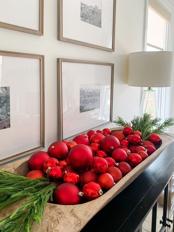 a stylish Christmas decoration of a wooden bowl filled wiht glossy and matte Christmas ornaments and evergreens