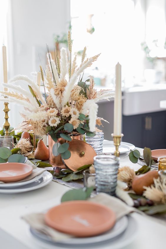 a stylish Thanksgiving tablescape with a neutral fresh and dried flower centerpiece with grass and greenery and some pears on the table