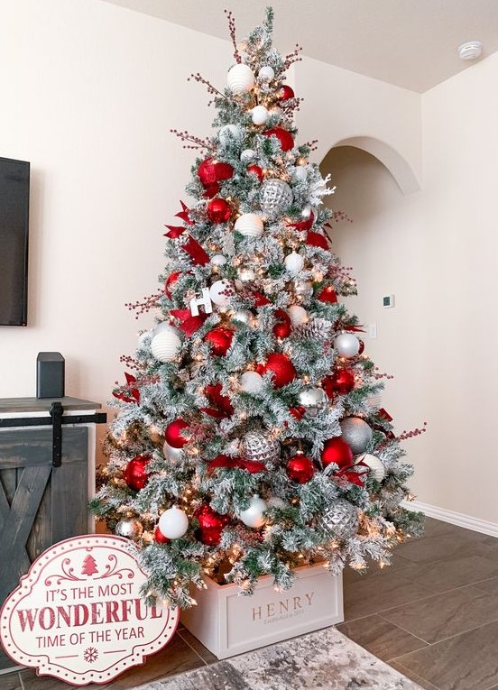 a stylish flocked Christmas tree decorated with silver, white and red ornaments, berry branches and letters
