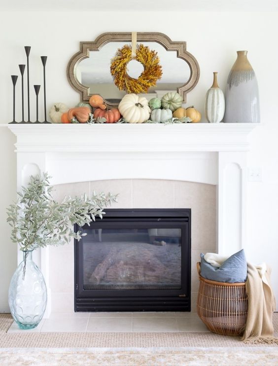 a stylish modern Thanksgiving mantel with a leaf wreath, neutral and pastel pumpkins and large vases