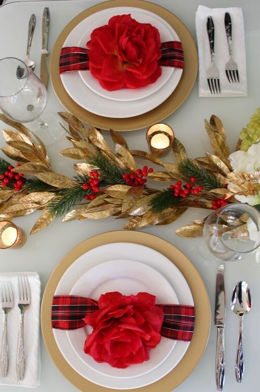 a stylish red and gold Christmas table with gold foliage, evergreens and berries, red blooms and candles