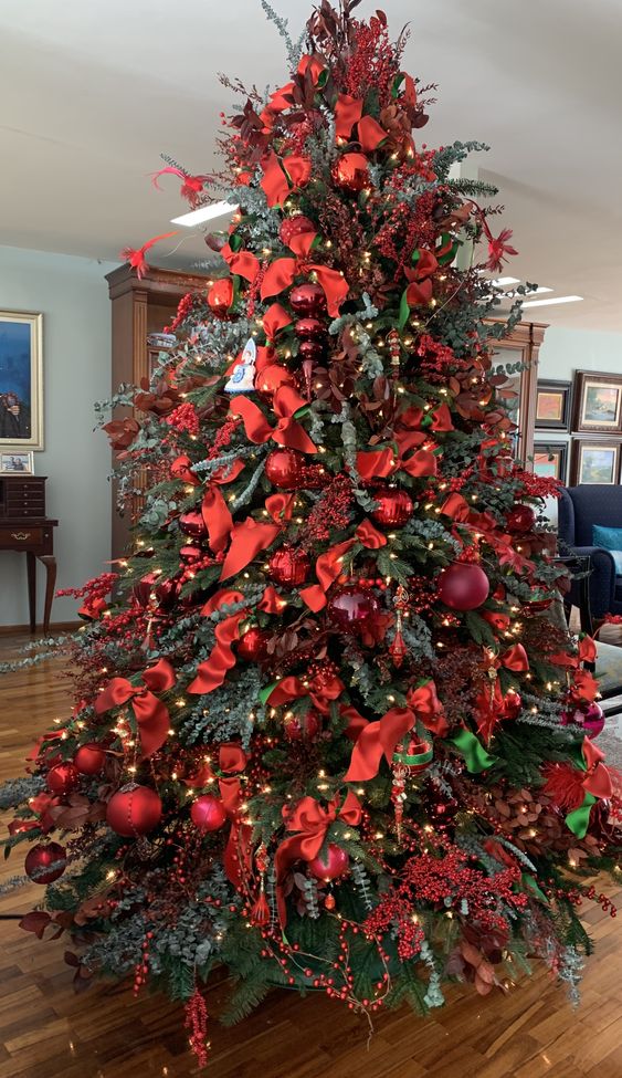 a super bold red Christmas tree with ornaments, bows, branches, ribbons and lights all covering the tree completely