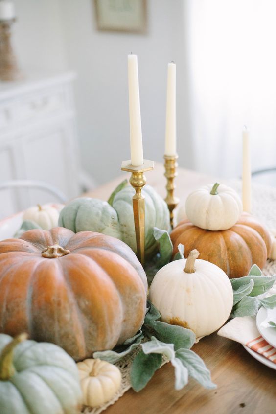 a super natural Thanksgiving centerpiece of various natural pumpkins, foliage and tall and thin candles in elegant candlesticks
