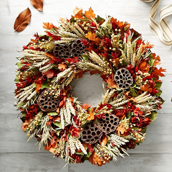 a unique fall or Thanksgiving wreath with bold leaves, wheat, lotus and some berries is a cool idea to go for