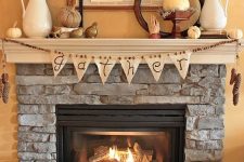 a vintage and rustic Thanksgiving mantel with a wooden bead and burlap garland plus pinecones in a bucket, mini pumpkins, feathers, ,etal gourds and signs