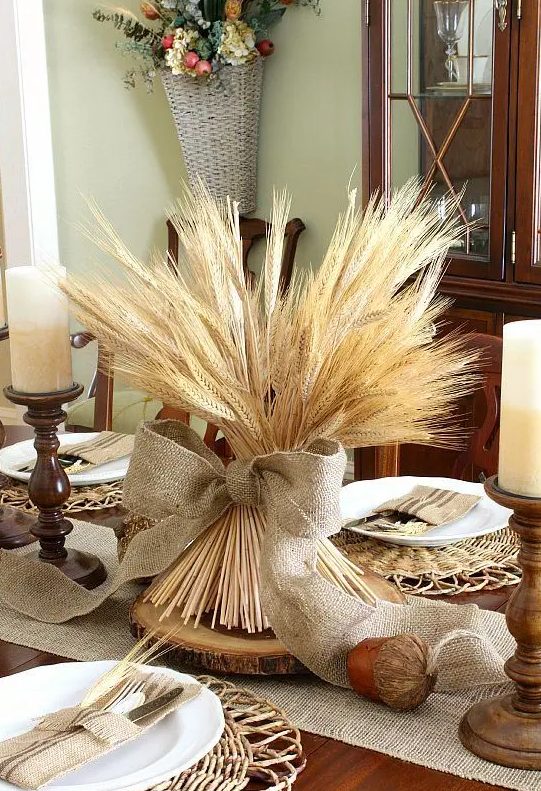 a vintage rustic Thanksgiving centerpiece of a bundle of wheat with a large burlap bow, a wood slice and a faux acorn